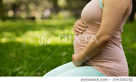 Pregnant caucasian woman doing yoga in the park. Close-up of the abdomen. Pregnant caucasian woman doing yoga in the park. Close-up of the abdomen. 104108192
