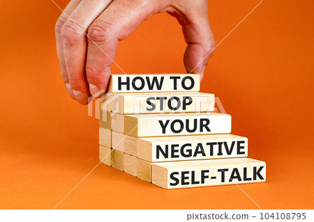 Stop negative self-talk symbol. Concept words How to stop your negative self-talk on wooden block. Psychologist hand. Beautiful orange background. Psychological negative self-talk concept. Copy space Stop negative self-talk symbol. Concept words How to stop your negative self-talk on wooden block. Psychologist hand. Beautiful orange background. Psychological negative self-talk concept. Copy space 104108795