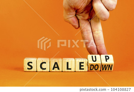 Scale up or down symbol. Concept words Scale up Scale down wooden cubes. Businessman hand. Beautiful orange table orange background. Business scale up or down concept. Copy space. 104108827