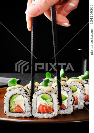 Female hand taking one Philadelphia roll from plate with chopsticks 104109363