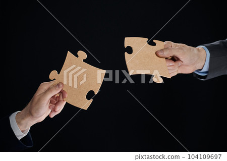 Close-up of business partners putting together white puzzle pieces on black background Close-up of business partners putting together white puzzle pieces on black background 104109697