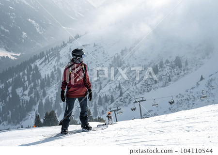 Tourist with snowboard on snow covered mountain with beautiful landscape in background during winter vacation, winter holiday travel concept 104110544