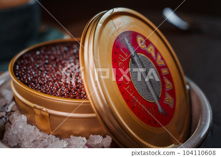 Black caviar in can placed on a plate with ice. A chocolate dessert styled as a caviar Black caviar in can placed on a plate with ice. A chocolate dessert styled as a caviar 104110608