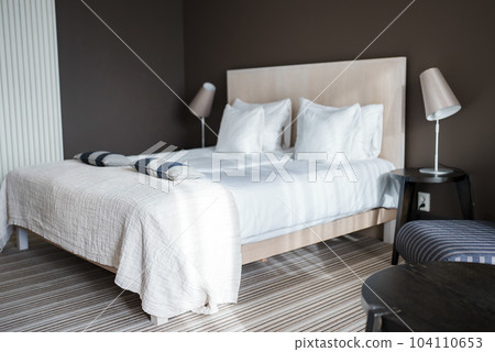 Lamps on night tables by cozy comfortable bed with cushions and blanket in elegant modern bedroom at luxurious hotel, alpine hotel interior design concept Lamps on night tables by cozy comfortable bed with cushions and blanket in elegant modern bedroom at luxurious hotel, alpine hotel interior design concept 104110653