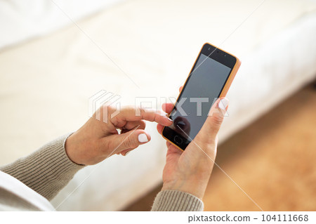 Close up of the hands from a middle aged woman sitting on a sofa at home and using her mobile phone. Close up of the hands from a middle aged woman sitting on a sofa at home and using her mobile phone. 104111668
