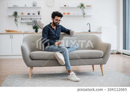 Person with tea and laptop resting on sofa in dining room Person with tea and laptop resting on sofa in dining room 104112065