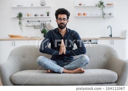 Adult stretching in yoga pose on couch in home interior Adult stretching in yoga pose on couch in home interior 104112067
