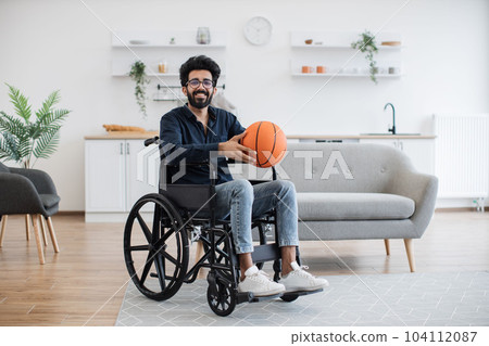 Adult in wheelchair holding basketball in room interior 104112087