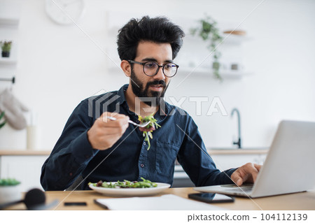 Freelancer dining while typing on computer in home workplace 104112139