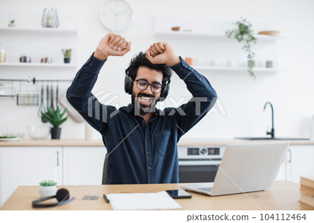 Male adult listening to songs via headphones in kitchen 104112464