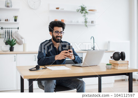Male texting message on phone in kitchen during working hour 104112597