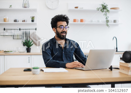 Freelancer operating laptop while sitting at desk in kitchen 104112937