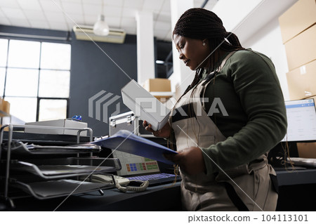 African american worker looking at white cardboard box, preparing customers orders at counter desk in storehouse. Stockroom employee wearing industrial overall during goods inventory African american worker looking at white cardboard box, preparing customers orders at counter desk in storehouse. Stockroom employee wearing industrial overall during goods inventory 104113101