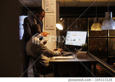 Executive managers analyzing financial statistics discussing investment strategy while working overhours in startup office. Businessmen planning brainstorming management ideas. Business concept Executive managers analyzing financial statistics discussing investment strategy while working overhours in startup office. Businessmen planning brainstorming management ideas. Business concept 104113126