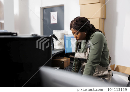 African american supervisor analyzing warehouse logistics on laptop computer, working at merchandise inventory in storage room. Storehouse employee preparing customers orders for shipping 104113139