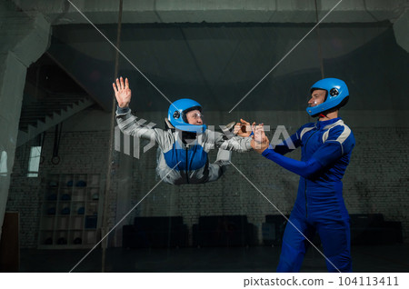 A male instructor teaches a woman how to fly in a wind tunnel. Free fall simulator. 104113411