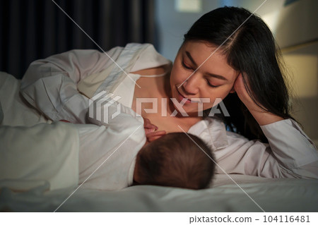 mother is breastfeeding a infant baby while lying and sleeping on bed at night mother is breastfeeding a infant baby while lying and sleeping on bed at night 104116481