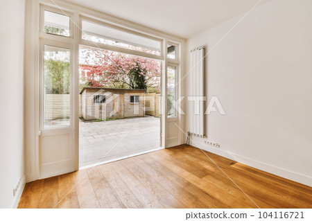 an empty room with wood flooring and sliding glass doors that open to the backyard patio area, which is surrounded by flowering trees 104116721