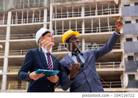Engineers in suits and hardhats discussing on building site 104116722