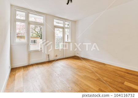 an empty living room with wood flooring and two windows looking out onto the street in front of the house 104116732