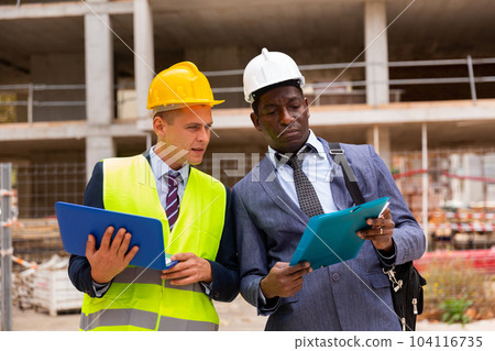 Architect and foreman must write documents and drawings on laptop with building construction Architect and foreman must write documents and drawings on laptop with building construction 104116735