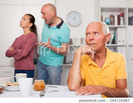 Elderly man sitting at table, unhappy family couple quarrelling Elderly man sitting at table, unhappy family couple quarrelling 104116967