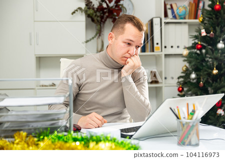 Exhausted male office worker sitting at his desk in Christmas decorated office Exhausted male office worker sitting at his desk in Christmas decorated office 104116973