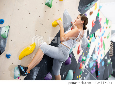 Young Europian woman climbs steep artificial wall in sports complex and trains endurance 104116975