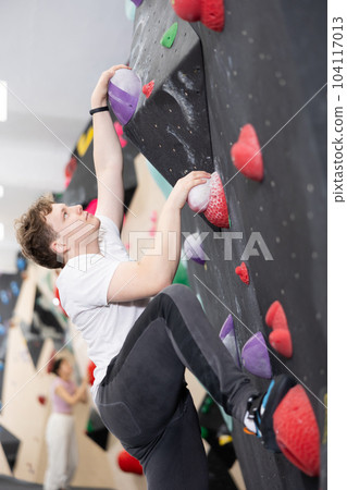 Teenage boy climbs steep artificial wall in sports complex and trains endurance Teenage boy climbs steep artificial wall in sports complex and trains endurance 104117013