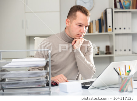 Man bookkeeper sitting at table and using laptop Man bookkeeper sitting at table and using laptop 104117123