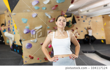Smiling young girl posing near climbing wall at bouldering gym after workout, feeling accomplished and energized Smiling young girl posing near climbing wall at bouldering gym after workout, feeling accomplished and energized 104117124
