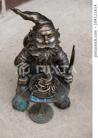 Dwarf eats pasta near restaurant. Small bronze figures of gnomes on the streets of Wroclaw. Europe Miniature bronze figure of a gnome. Symbol of Wroclaw 104121614