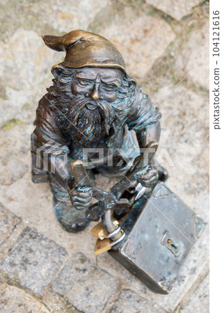 Dwarf with a padlock near bridge. Small bronze figures of gnomes on the streets of Wroclaw. Europe Miniature bronze figure of a gnome. Symbol of Wroclaw 104121616