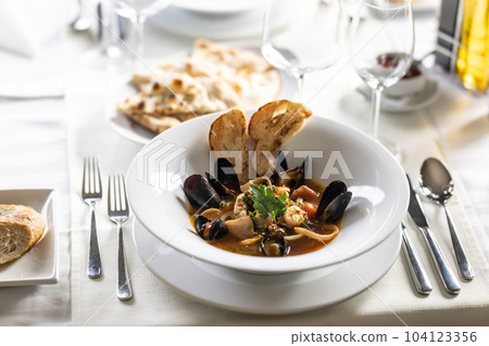 Seafood soup with mussels, fish, shrimp and other served with pastry on a nice table setting 104123356