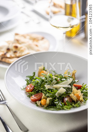 Rocket salad with parmesan, physalis and cherry tomatoes next to flat bread Rocket salad with parmesan, physalis and cherry tomatoes next to flat bread 104123365