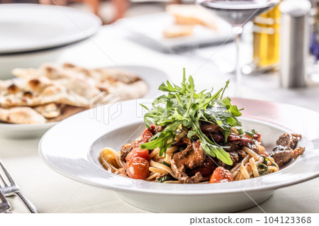 Linguine with tomatoes and tender beef meat served in a plate and topped with rocket salad Linguine with tomatoes and tender beef meat served in a plate and topped with rocket salad 104123368