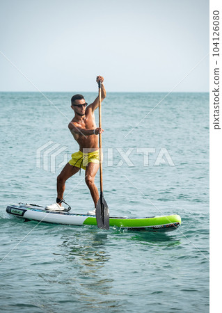 a sporty guy swims on a sup board with a paddle on the sea during the day against a beautiful sky 104126080
