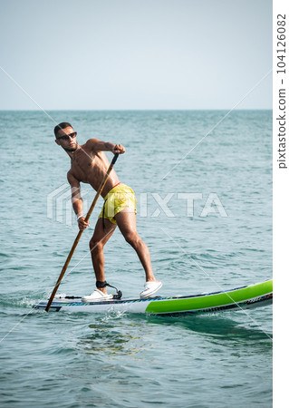 a sporty guy swims on a sup board with a paddle on the sea during the day against a beautiful sky 104126082