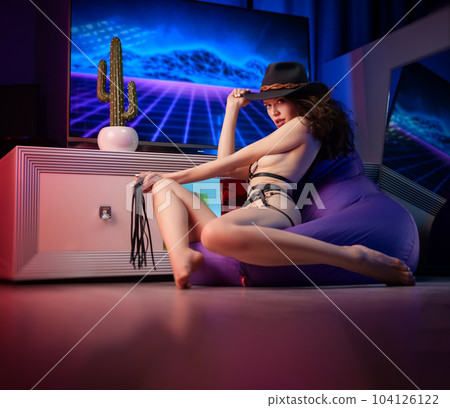 sexy naked girl in a hat and leather straps bdsm in a room with neon flowers 104126122