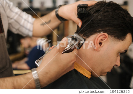 Handsome bearded man cutting hair of confident male client in berber shop Handsome bearded man cutting hair of confident male client in berber shop 104126235