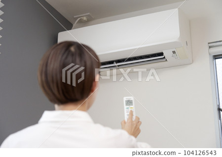 Back view of a woman using the air conditioner remote control Back view of a woman using the air conditioner remote control 104126543