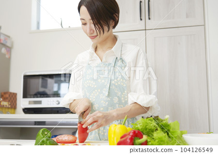 Middle aged woman cutting tomatoes in the kitchen Middle aged woman cutting tomatoes in the kitchen 104126549