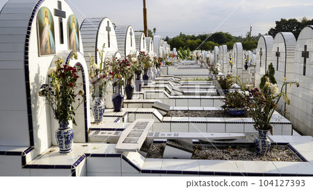 The public cemetery contains identical white ceramic graves with flowers. The public cemetery contains identical white ceramic graves with flowers. 104127393