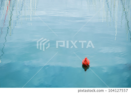 Orange buoy floating on the waves of the sea surface in the bay. Reflection of yacht masts in the water. The concept of the safety of human life. 104127557