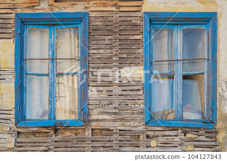 Facade of a crumbling old wooden house with blue windows. Abandoned houses of the old city idea for background 104127843