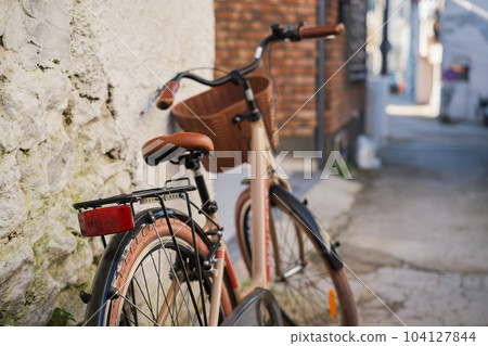 Modern bike in retro style on the street in the old town, selective focus. Cozy old street idea for decor and interior design. Modern bike in retro style on the street in the old town, selective focus. Cozy old street idea for decor and interior design. 104127844