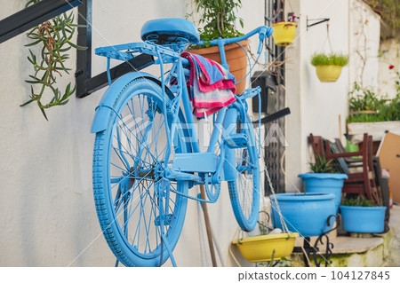 Old bicycle in a cafe on the street in the old town. Cozy street with flowers and cafe on the mediterranean coast. Facade decor of a coffee shop with a bicycle. Old bicycle in a cafe on the street in the old town. Cozy street with flowers and cafe on the mediterranean coast. Facade decor of a coffee shop with a bicycle. 104127845