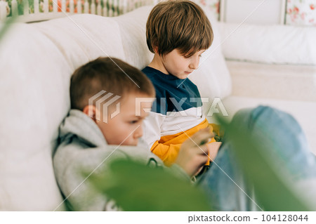 Cheerful two Childs boys playing online game, watching video on cellphone. Smiling kids using funny mobile apps, enjoying free leisure time at home on couch. Brothers play together at phone Cheerful two Childs boys playing online game, watching video on cellphone. Smiling kids using funny mobile apps, enjoying free leisure time at home on couch. Brothers play together at phone 104128044