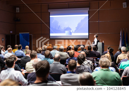 Speaker giving a talk in conference hall at business meeting event. Rear view of unrecognizable people in audience at the conference hall. Business and entrepreneurship concept. 104128845