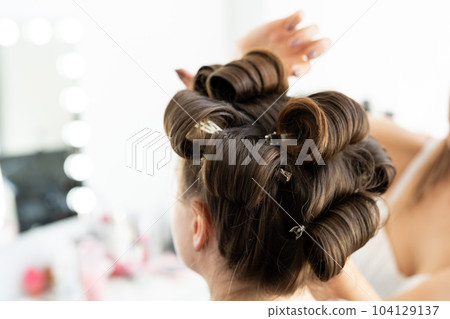 The hairdresser curls the model's hair. Curling iron for curling hair close-up. The hairdresser curls the model's hair. Curling iron for curling hair close-up. 104129137